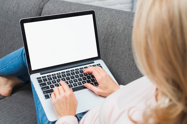 Foto nahaufnahme von blondinen sitzend auf sofa unter verwendung des laptops mit leerem weißem bildschirm