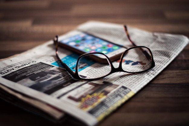 Foto nahaufnahme von brille und mobiltelefon auf zeitung über tisch