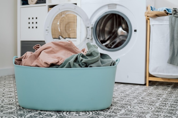 Nahaufnahme von bunten Kleidern in einer großen Schüssel offener Waschmaschine, die im Hintergrund steht