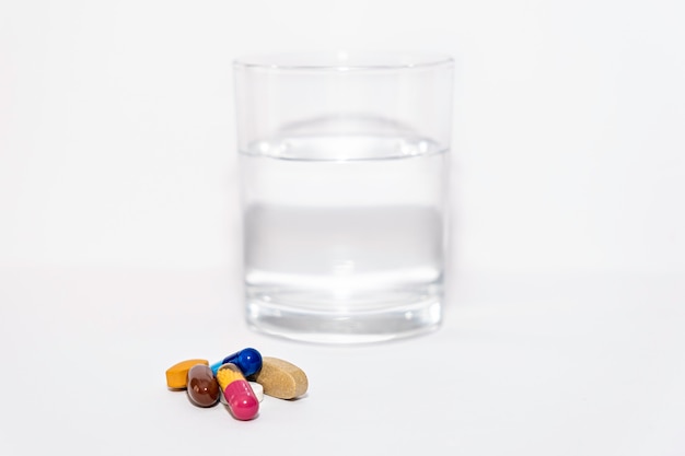 Nahaufnahme von bunten Pille Kapsel Vitamine Ergänzung mit Glas Wasser auf weißer Oberfläche in der Nähe