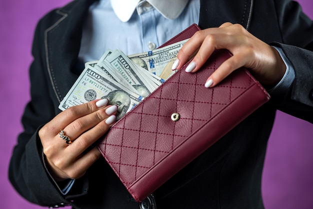 Nahaufnahme von den Händen einer Frau, die einen Hundert-Dollar-Schein in ihre Handtasche steckt, konzentriert sich auf die Handtasche, Geld, Dollar in der Brieftasche.