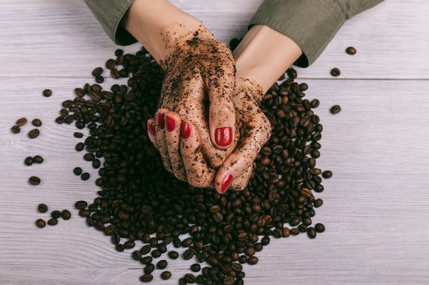 Nahaufnahme von den weiblichen Händen beschichtet mit Peeling und Kaffeebohnen