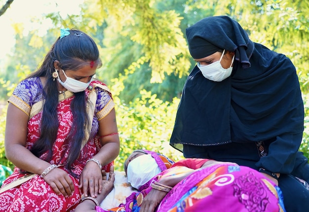 Nahaufnahme von drei indischen Frauen, von denen eine liegt und die alle bei Tageslicht Gesichtsmasken tragen