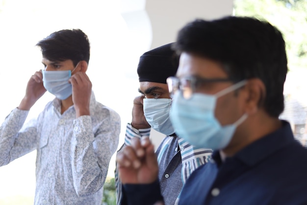 Nahaufnahme von drei indischen Männern, die eine medizinische Maske im Hintergrund der Klinik tragen