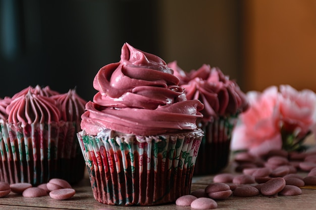 Nahaufnahme von drei Schokoladencupcakes mit rosa Buttercreme. Neben Ruby Schokoladen Callets. Brauner und orange Hintergrund.