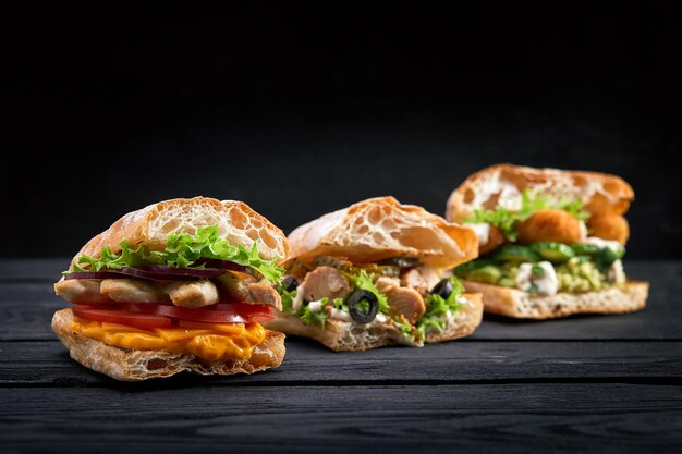Nahaufnahme von drei verschiedenen appetitvollen Sandwiches oder Burgern auf hölzernem Hintergrund