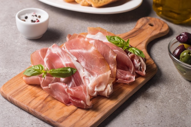 Nahaufnahme von dünnen Scheiben Prosciutto mit gemischten Oliven