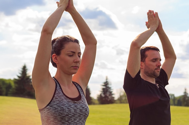 Nahaufnahme von einem gesunden Mann und einer gesunden Frau, die im sonnigen Sommerpark Yoga machen Fitness und gesunder Lebensstil
