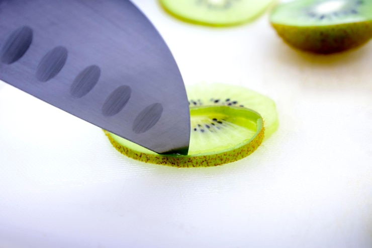 Foto nahaufnahme von einem messer, das kiwi auf dem tisch schneidet