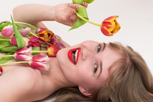 Nahaufnahme von einem Porträt einer glücklichen Frau mit Frühlings-Tulpenblumen für den Frauentag auf der Brust und in der Hand