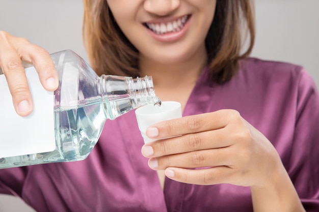 Nahaufnahme von einer jungen Frau, die Mundwasser gegen einen grauen Hintergrund hält