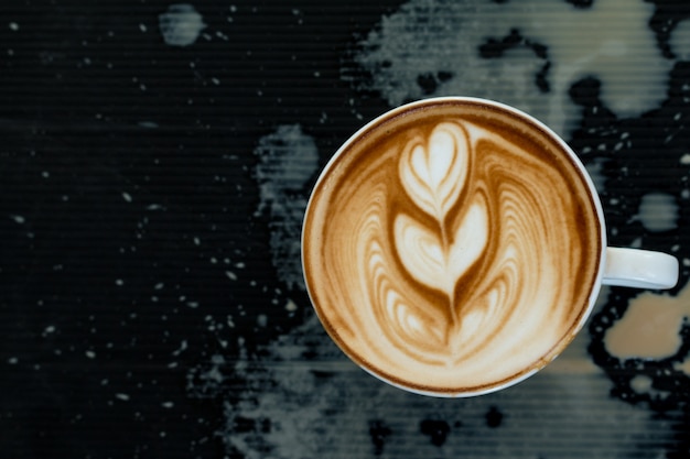Nahaufnahme von einer Tasse Latte Art heißen Kaffee über Kaffee Tropfen auf schwarzem Kunststoff-Karton Hintergrund oben auf Kaffee Shop-Tabelle