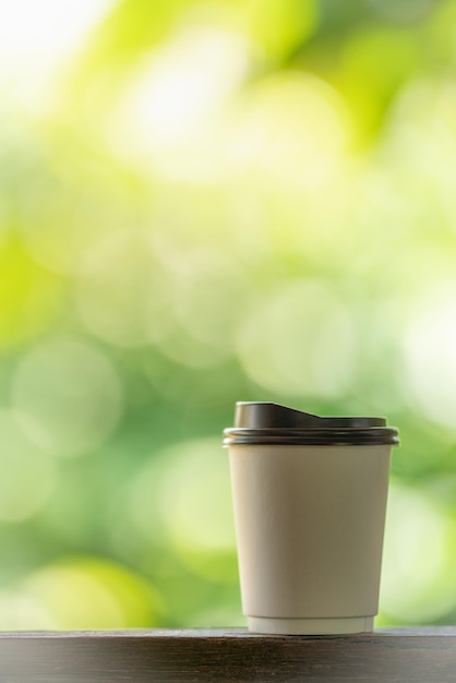 Nahaufnahme von Einweg-Pappbecher heißen Kaffee auf Holzstange mit grünem Naturhintergrund.