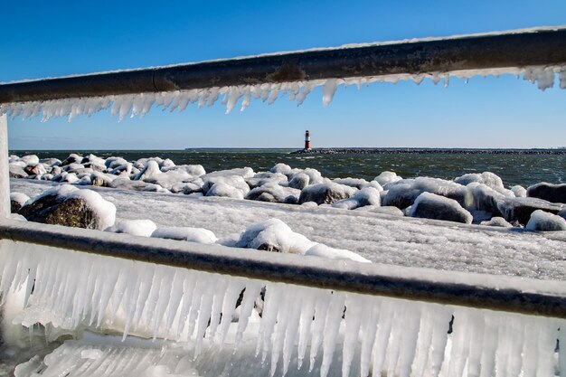 Nahaufnahme von Eisstielen auf einem Geländer am Meer vor einem klaren blauen Himmel