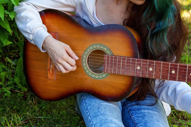 Nahaufnahme von Frauenhänden, die Akustikgitarre auf Park- oder Gartenhintergrund spielen. Jugendlich Mädchen, das lernt, Lied zu spielen und Musik zu schreiben. Hobby, Lifestyle, Entspannung, Instrument, Freizeit, Bildungskonzept