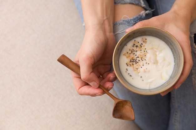 Nahaufnahme von Frauenhänden, die eine Tasse mit Bio-Joghurt mit Kokos- und Chiasamen halten