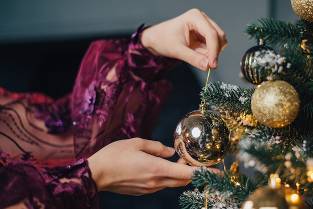 Nahaufnahme von Frauenhänden, die Weihnachtsbaum mit Kugeln schmücken, zurückhaltend