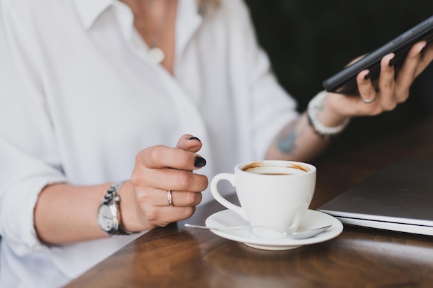 Nahaufnahme von Frauenhänden mit einem Telefon und einer Tasse Kaffee an einem Tisch in einem Café