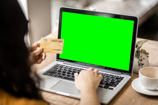 Nahaufnahme von freiberuflichen Geschäftsfrauen Hand mit Kreditkarten lässiges Arbeiten mit Laptop-Computer mit einem leeren grünen Bildschirm im Café wie der Hintergrund, Online-Zahlungseinkauf