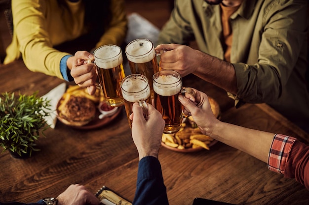 Nahaufnahme von Freunden, die in einer Kneipe mit Bier anstoßen