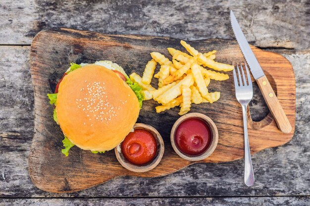 Nahaufnahme von frischem Burger mit Pommes Frites auf Holztisch mit Schalen mit Tomatensauce Lifestyle-Essen