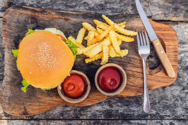 Nahaufnahme von frischem Burger mit Pommes Frites auf Holztisch mit Schalen Tomatensauce. Lifestyle-Lebensmittel.