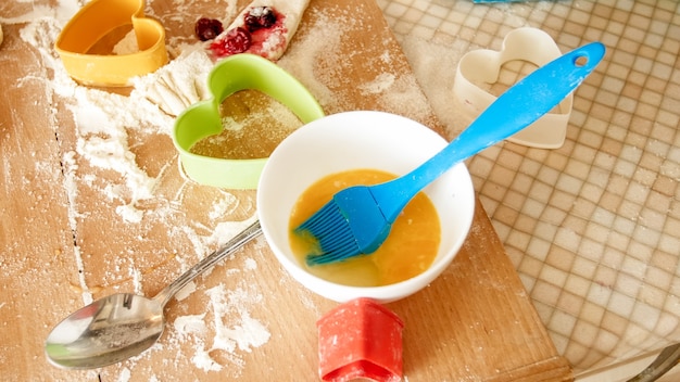 Nahaufnahme von frischem Teig, Eiern, Milch und vielen Werkzeugen zum Backen und Kochen, die auf der großen Küchentheke aus Holz liegen