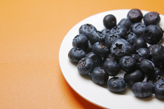 Nahaufnahme von frischen blauen Beeren auf einem Teller auf orangefarbenem Hintergrund