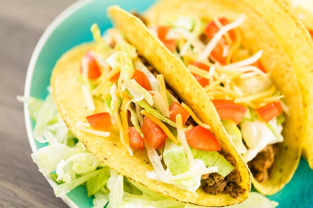 Nahaufnahme von frischen Rindfleisch-Tacos in harter gelber Mais-Taco-Schale mit Sauerrahm und geriebenem Käse.