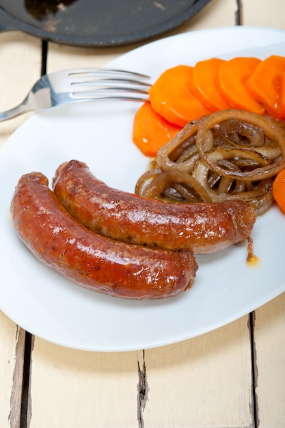Nahaufnahme von frischen Würstchen mit Zwiebeln und Karotten auf einem Teller auf dem Tisch