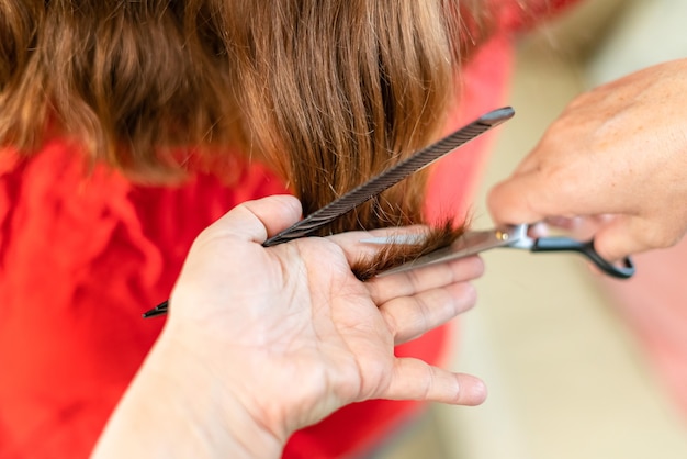 Foto nahaufnahme von friseurhänden, die zu hause braune haare schneiden. professioneller stylist, der spliss schneidet.