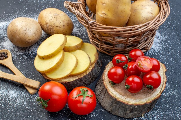 Nahaufnahme von ganzen und gehackten frischen Kartoffeln und Tomaten auf Holzbrettpfeffer auf schwarz-weißem Mischfarbenhintergrund