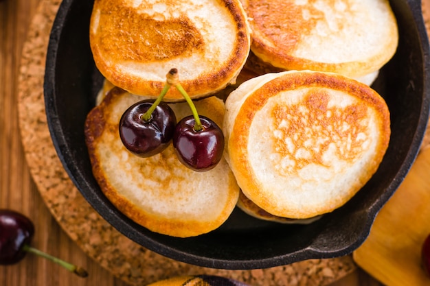 Nahaufnahme von gebratenen Pfannkuchen in einer Eisenwanne und in reifen Kirschen