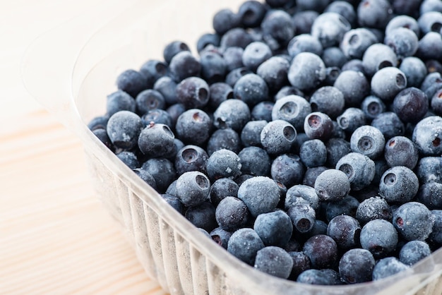 Nahaufnahme von gefrorenen Blaubeeren in transparenter Kunststoffschale auf weißem Holztisch Vegetarische gesunde Ernährung vom Sommer für den Winter