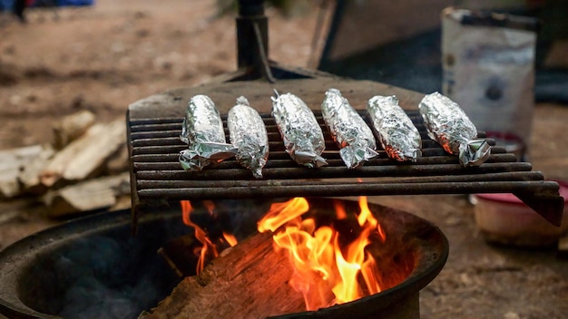 Nahaufnahme von gegrillten, mit Folie bedeckten Zuckermaiskolben beim Sommerpicknick im Wald