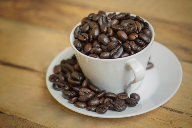 Nahaufnahme von gerösteten Kaffeebohnen auf einer Tasse und Untertasse über einem Holztisch, aufgenommen im Studio