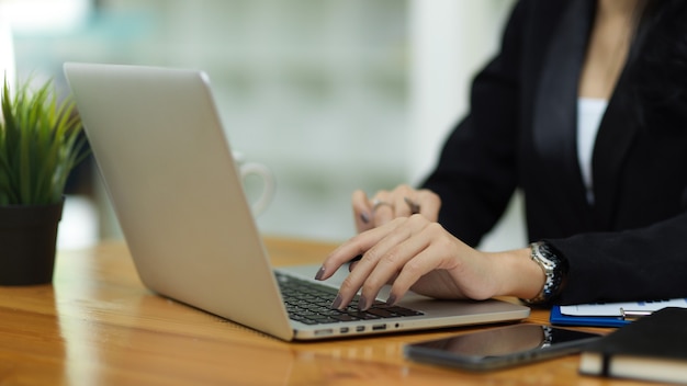 Nahaufnahme von Geschäftsfrauen in schwarzen Anzughänden, die auf der Laptop-Tastatur am Arbeitsplatz tippen