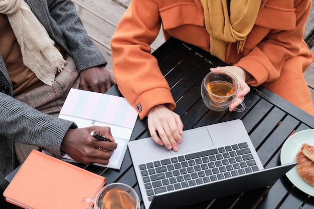 Nahaufnahme von Geschäftsleuten, die am Tisch sitzen, Tee trinken und am Laptop arbeiten