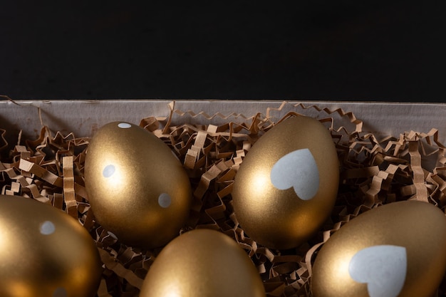Nahaufnahme von Gold-Eiern in Papierkisten auf schwarzem Hintergrund