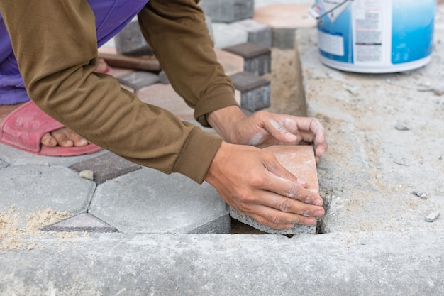 Nahaufnahme von Händen der Arbeitskraft arbeitend an der Platzierung des Steinblocks für Fußweg. Bau Arbeitskonzept.