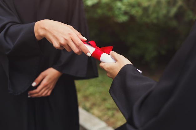 Nahaufnahme von Händen, die Abschlusszeugnis geben, zwei Studenten, die draußen Diplom halten, Kopienraum. Bildung, Qualifizierungskonzept