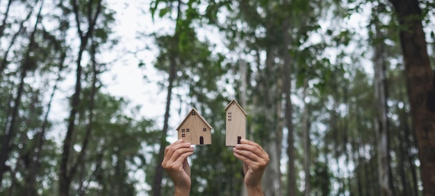 Nahaufnahme von Händen, die Holzhausmodelle mit Naturhintergrund halten und zeigen