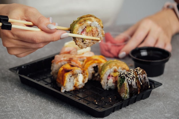 Nahaufnahme von Händen, die Sushi-Rolle mit Stäbchen halten