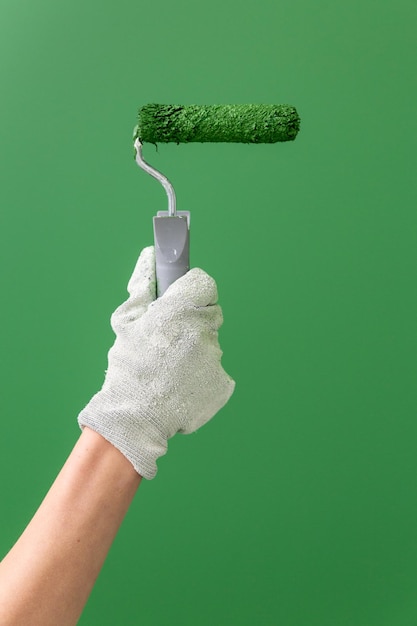 Nahaufnahme von Händen in Arbeitshandschuhen, die eine mittelgroße Rolle mit grüner Farbe vor der grünen Wand halten