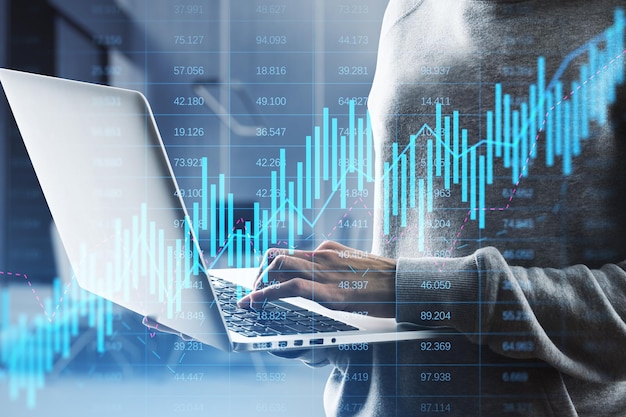 Nahaufnahme von Händen mit Laptop mit leuchtendem Candlestick-Forex-Diagramm auf verschwommenem Hintergrund im Bürointerieur Handel mit Aktien und globalem Finanzkonzept Doppelbelichtung