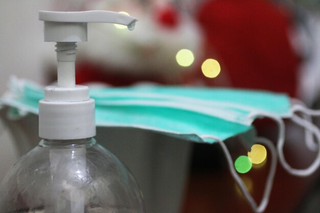 Foto nahaufnahme von handdesinfektionsmittel und gesichtsmasken im hintergrund von weihnachtslichtern