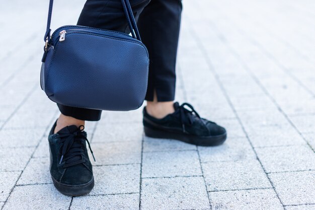 Nahaufnahme von Handtaschen- und Frauenbeinen in den Turnschuhen auf dem Bürgersteig.