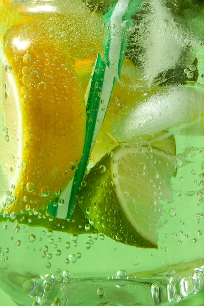 Nahaufnahme von hausgemachtem frischem Cocktail mit Eisscheiben von Limette und Zitronenblatt von Minze mit Plastik