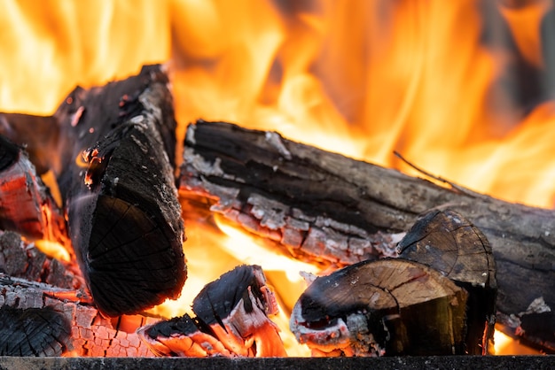 Nahaufnahme von hell brennenden Holzstämmen mit gelben heißen Feuerflammen in der Nacht.