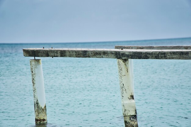 Nahaufnahme von Holzpfosten, Resten eines alten Piers am Strand und türkisblauem Wasser des karibischen Meeres.